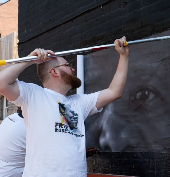 Isaac Campbell pasting on picture of Paul Rusesabagina onto wall