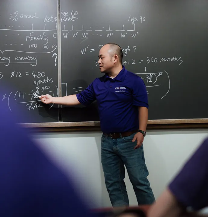 Professor writing on chalkboard. 