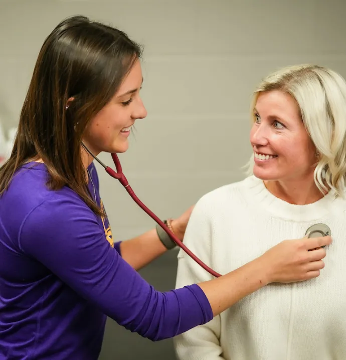 Athletic training student checks patients heart with stethoscope 