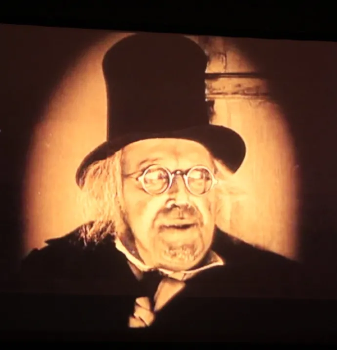 Man with a top hat and glasses in dim light looking off to the side