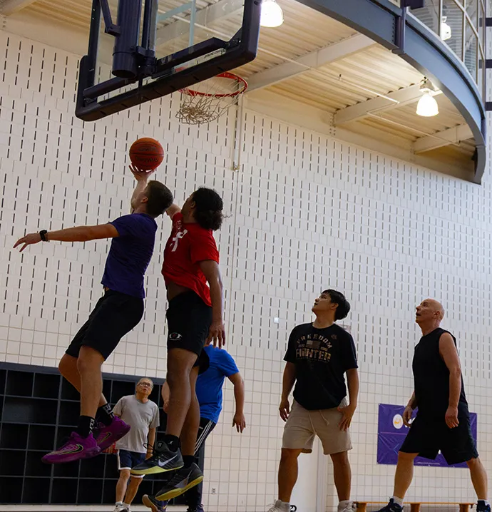 UNI students and faculty play basketball together as a student goes up for a layup.