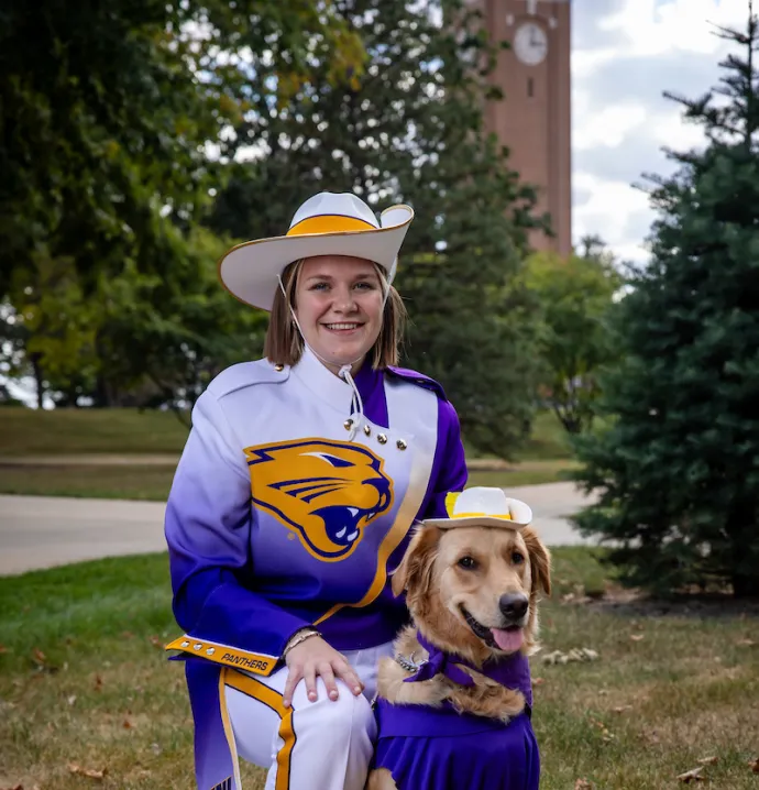 Gabi Riessen with golden retriever Winnie, both dressed in Panther Marching Band gear