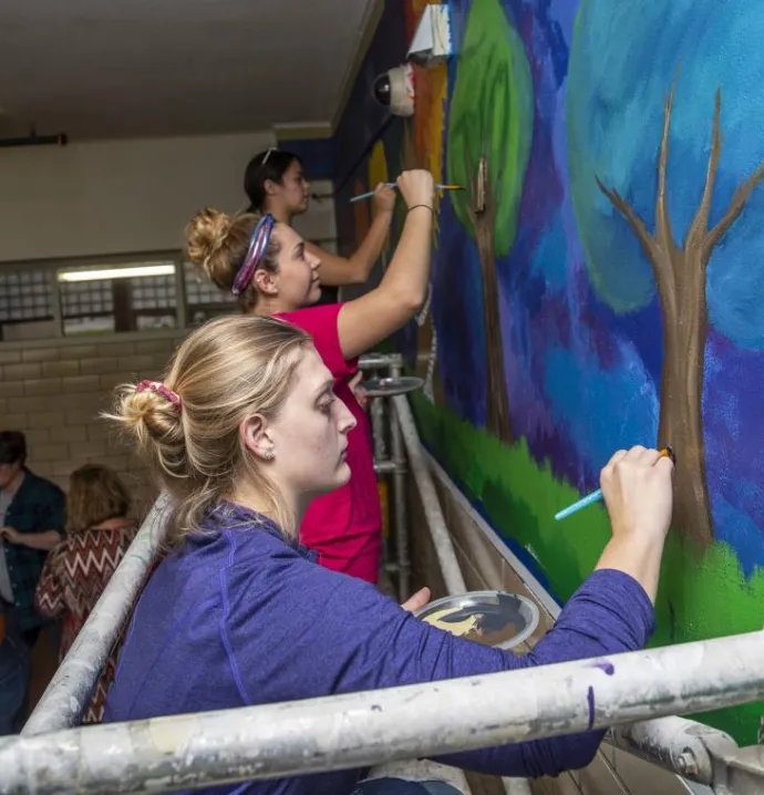 UNI students help paint a mural at Expo High School.
