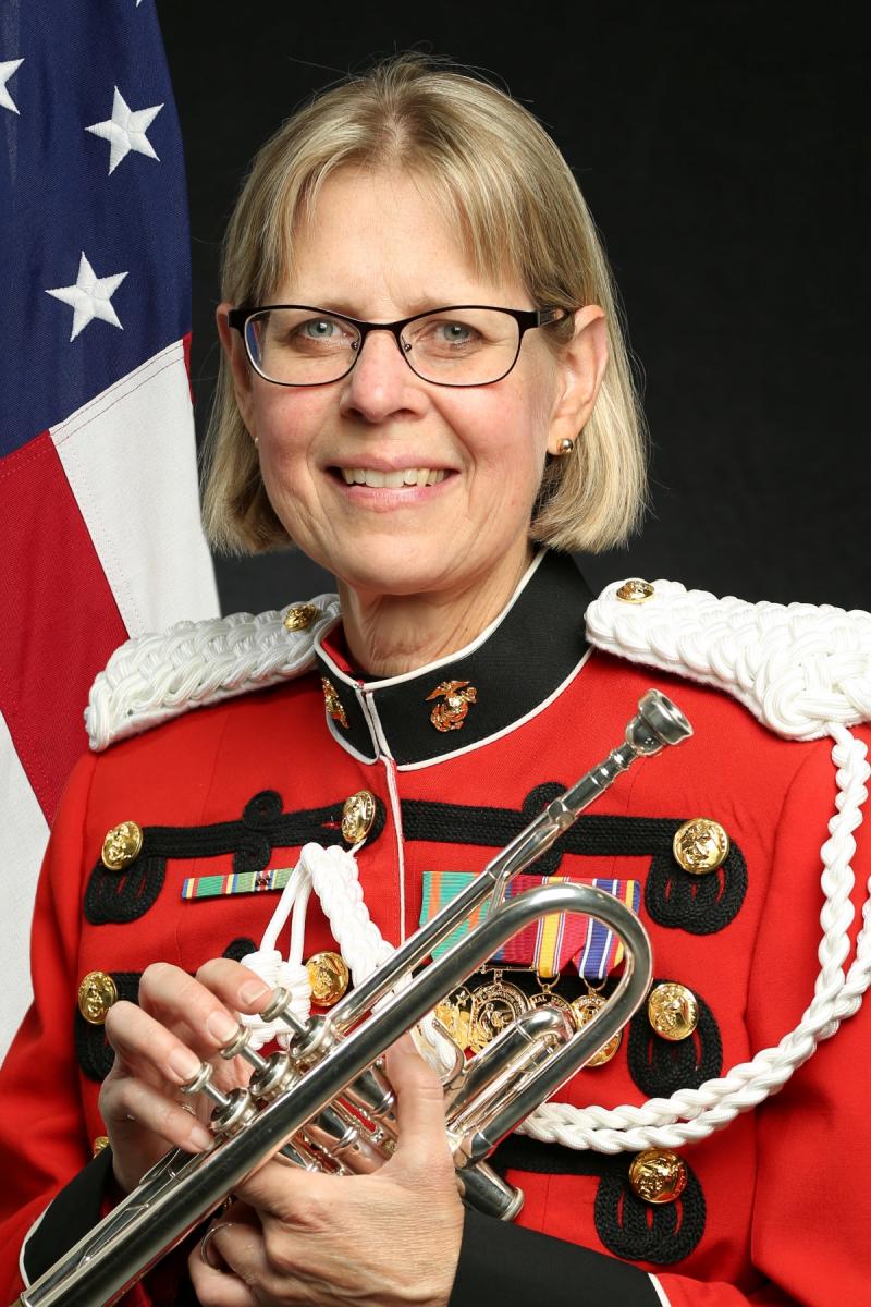 Susan Rider posing in uniform with trumpet in front of American flag